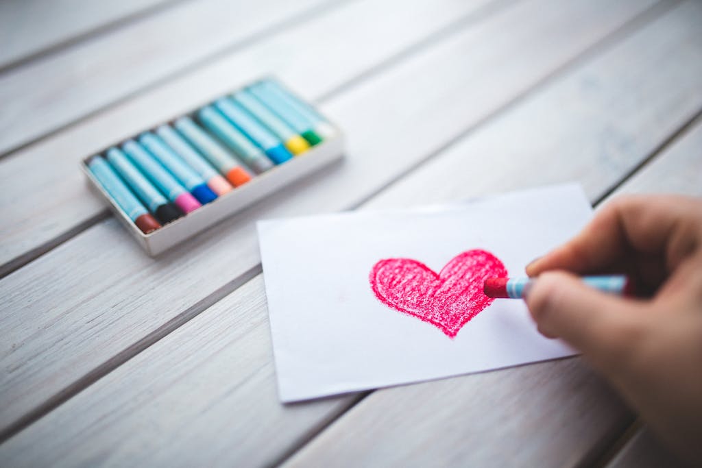 Hand with oil pastel draws the heart